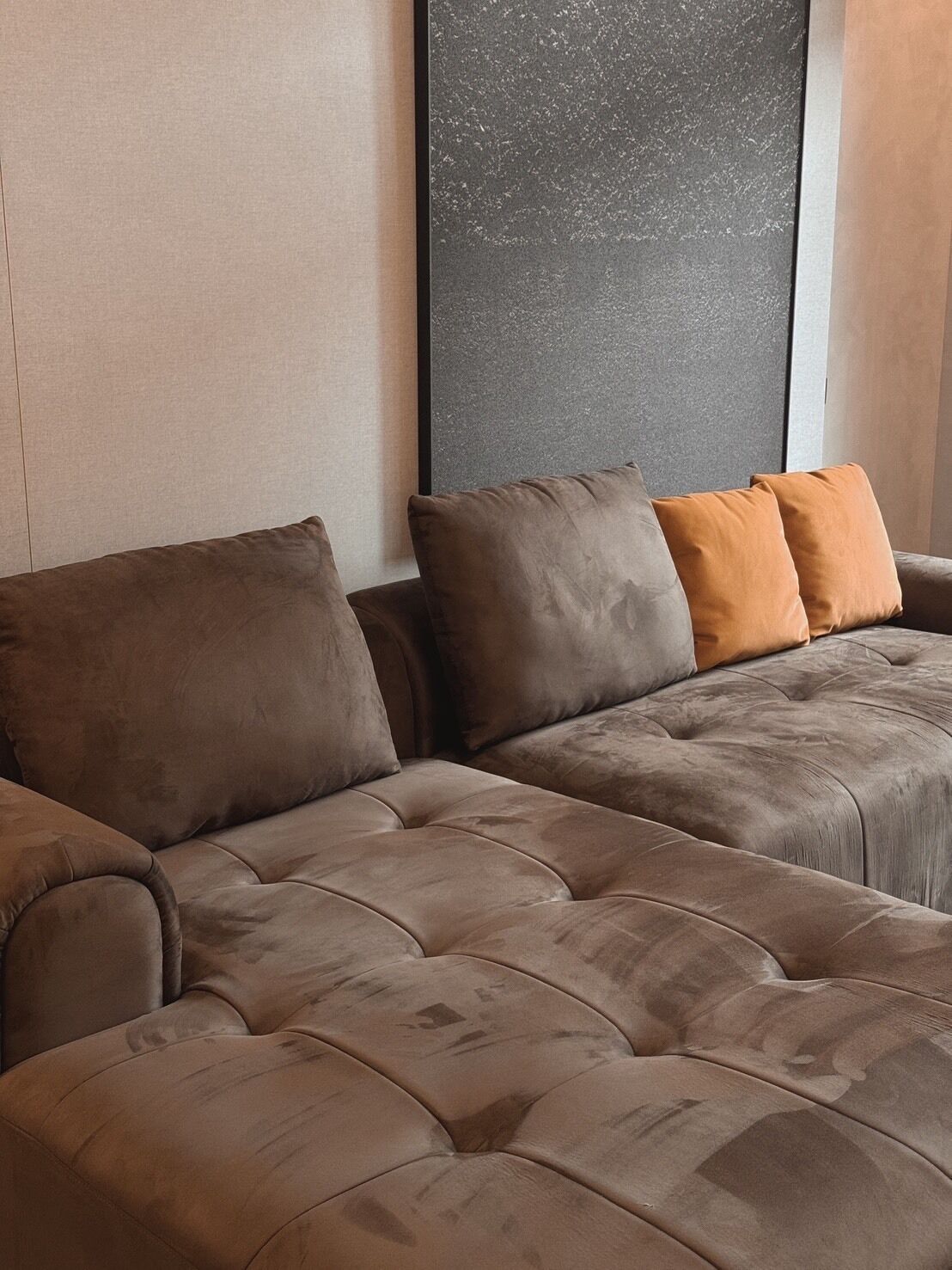 A sectional sofa with multiple cushions in a neutral color palette, positioned against a textured wall.