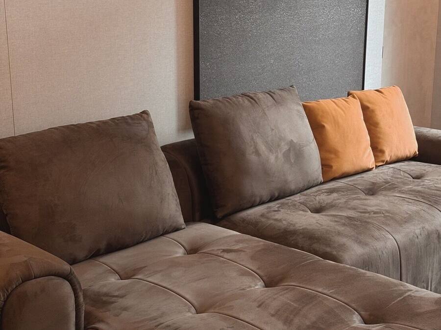 A sectional sofa with multiple cushions in a neutral color palette, positioned against a textured wall.