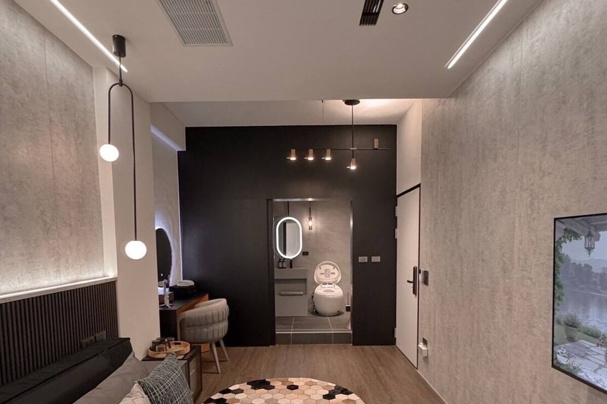A modern hallway with a sofa, a rug, and a bathroom with a mirror and toilet visible.