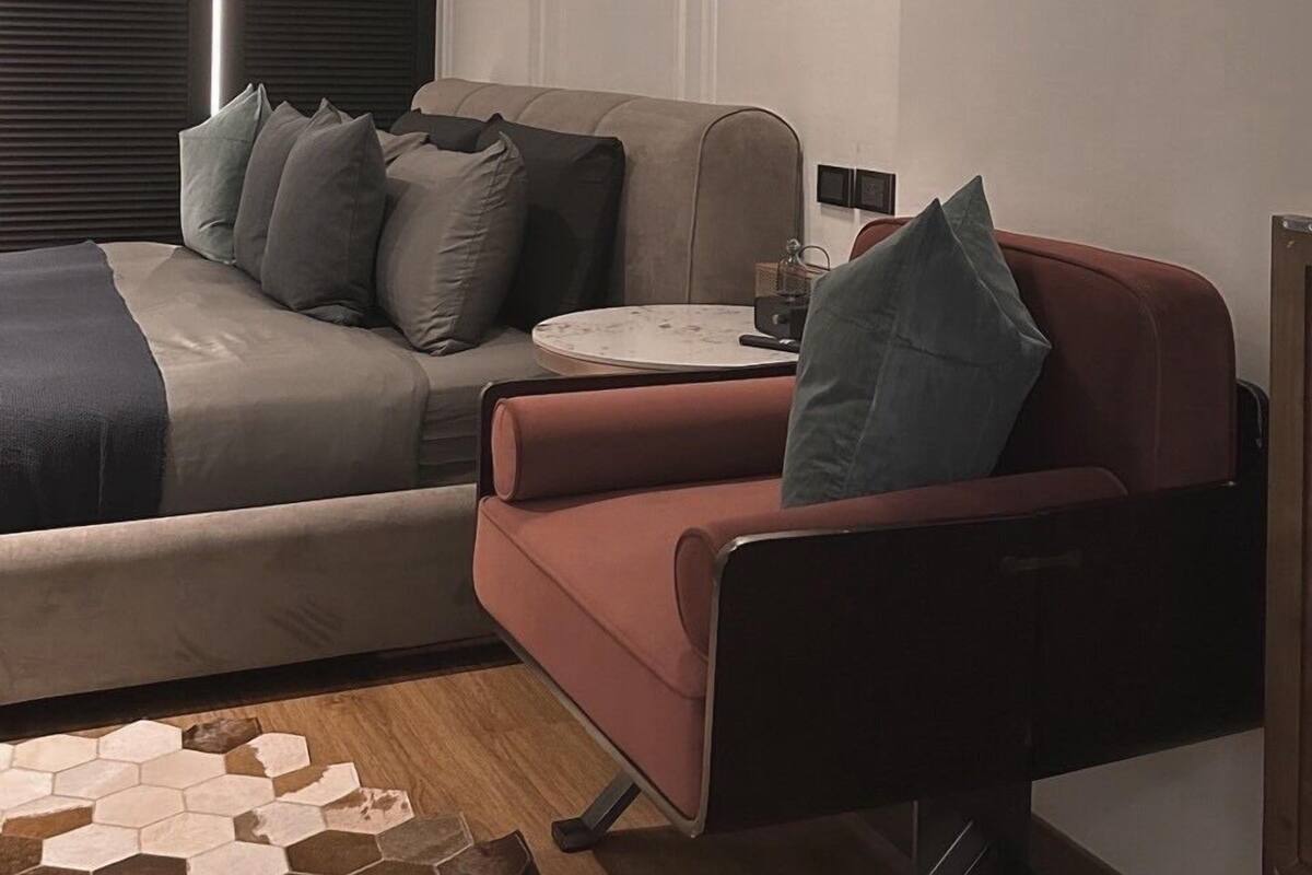 A modern living room with a sofa, armchair, and a coffee table. There is a ceiling vent and a hanging light fixture.