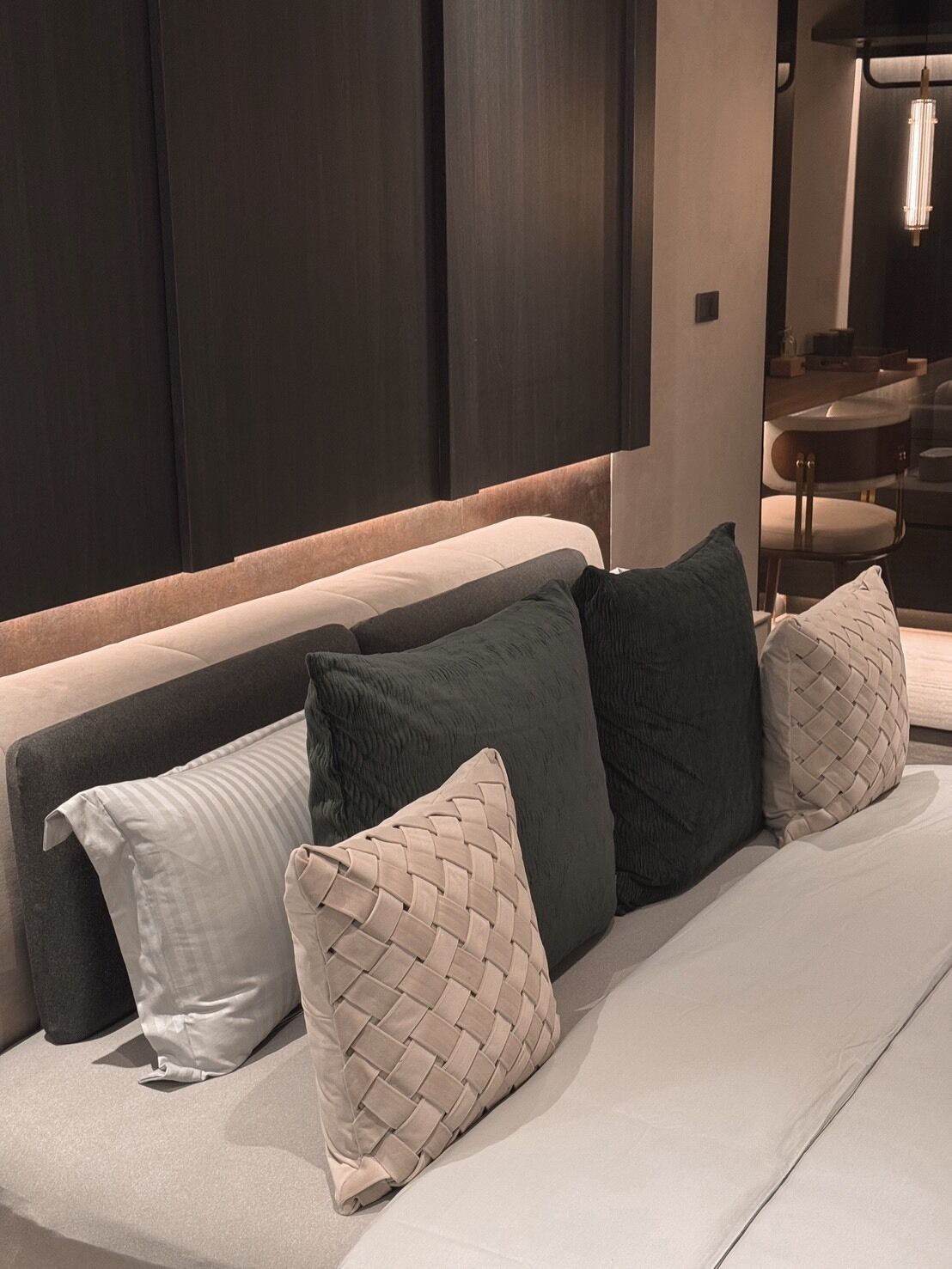 A modern hotel room with a large bed, dark wooden headboard, and a dining area visible through a glass partition.