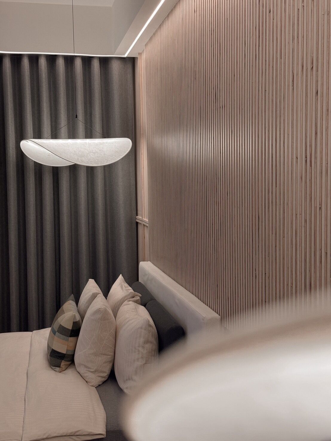 Un dormitorio moderno con una cama, una lámpara colgante y un panel de pared de madera.