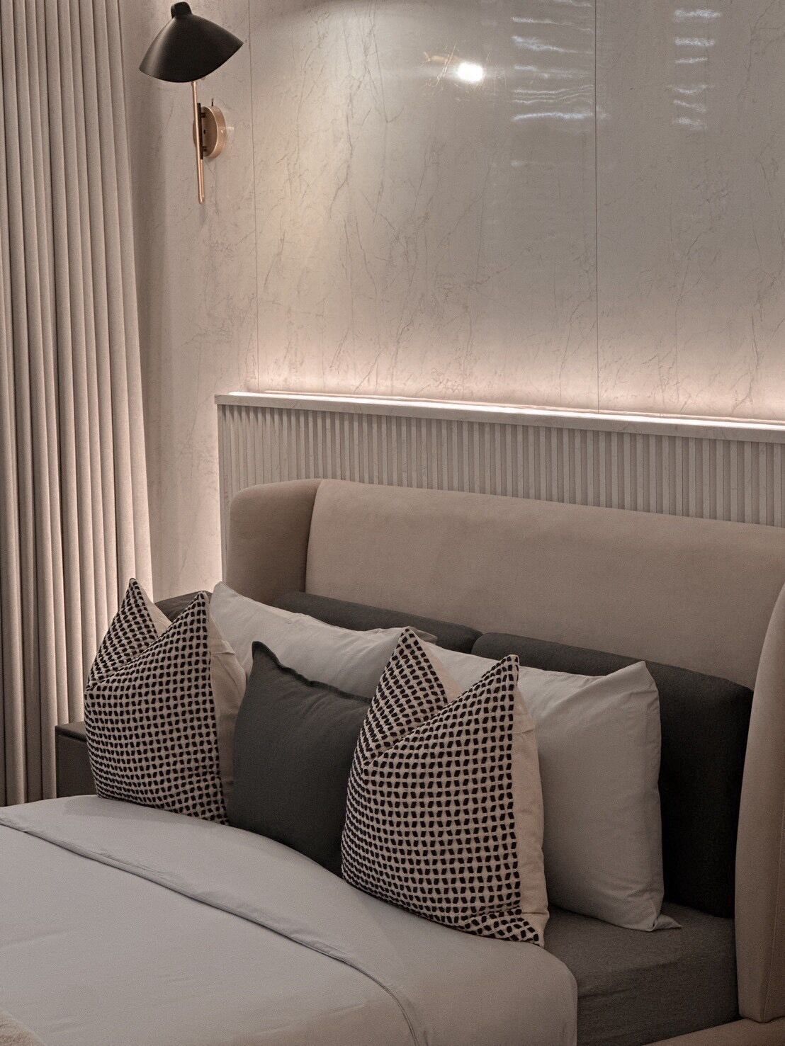 Un dormitorio moderno con una cama grande, cabecera con iluminación integrada y una lámpara de pared.
