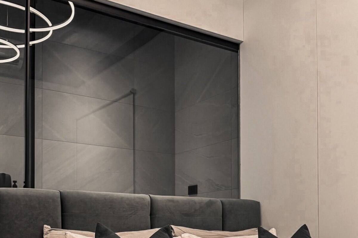 A modern bedroom with a large bed, dark headboard, and a large window.