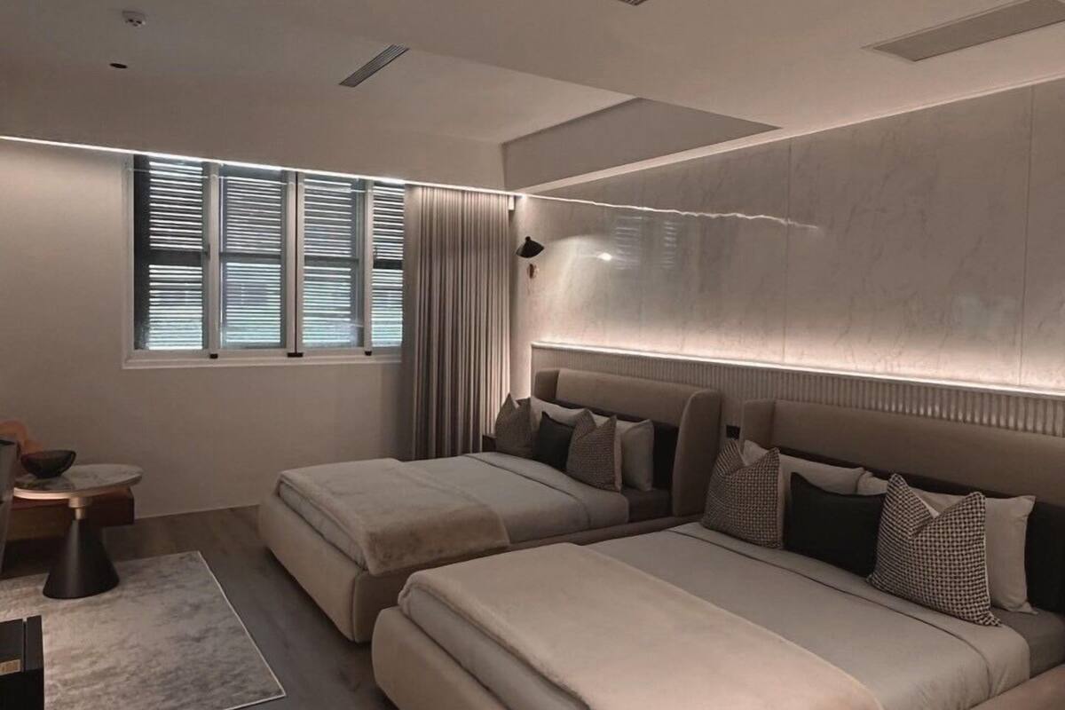A modern bedroom with two beds, a large window, and a built-in headboard.