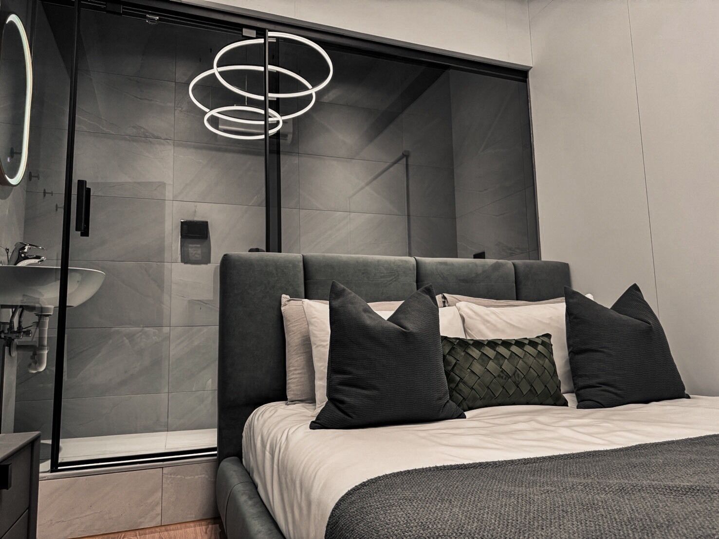 A modern bedroom with a large bed, a glass shower enclosure, and a pendant light.