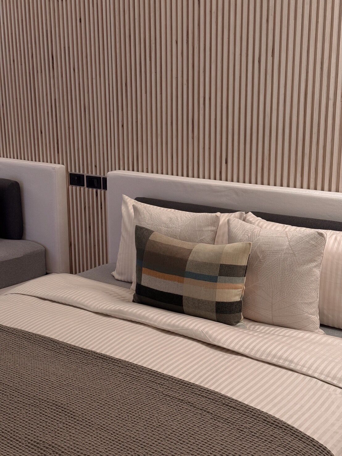 A modern hotel room with a bed, a bedside table, and a wall with vertical wooden slats.