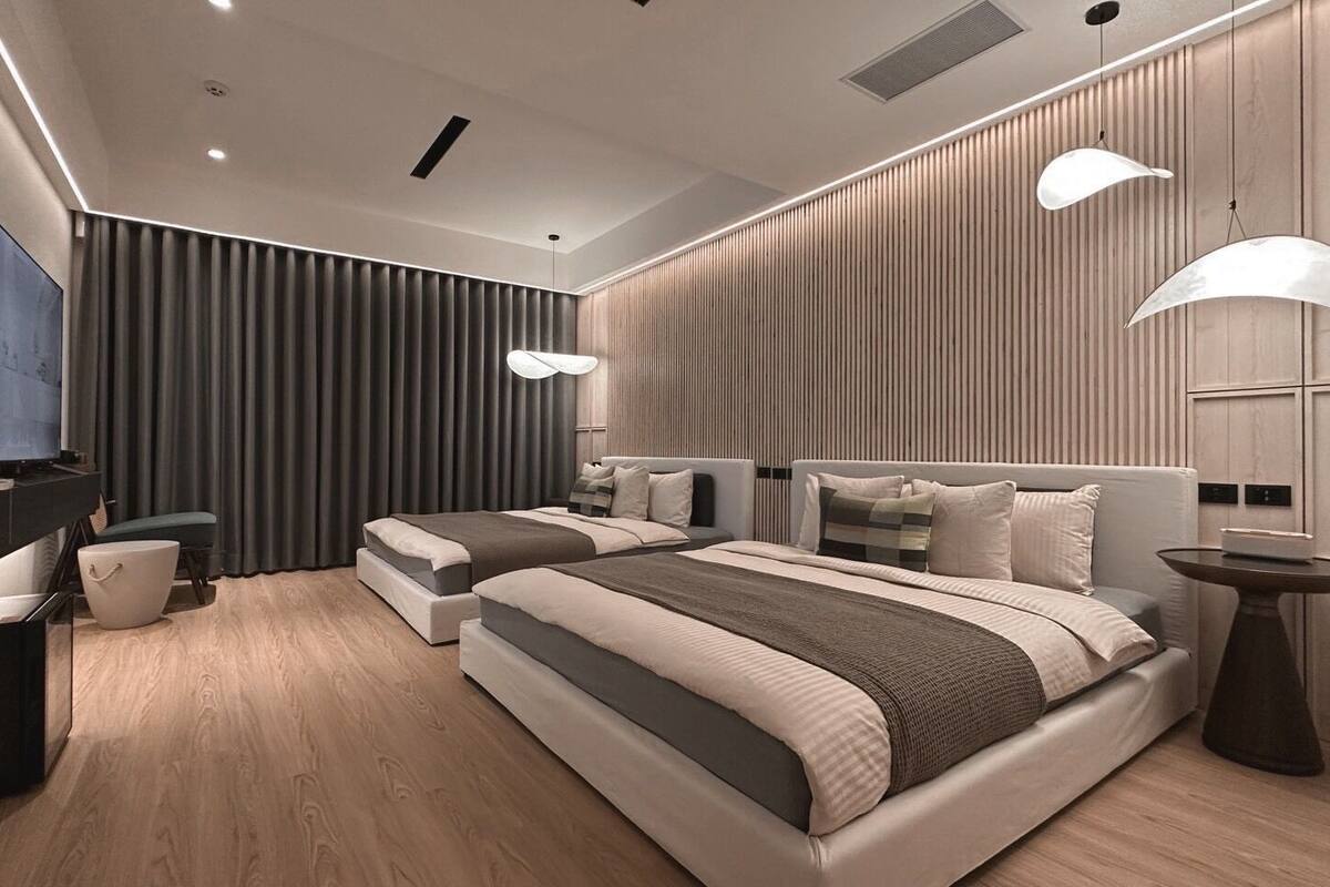A modern bedroom with two beds, a TV, and a desk.