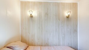Een slaapkamer met een houten hoofdbord, twee wandlampen, en een bed met een lichtkleurige dekbedovertrek en kussens.