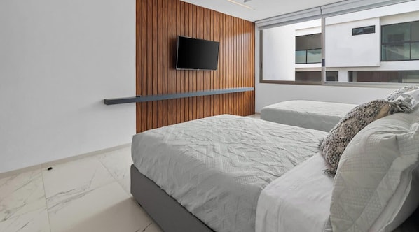 A modern bedroom with a wooden panel wall, a mounted TV, a ceiling fan, and a large window offering a view of the building's exterior.