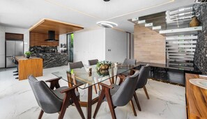 Una cocina moderna con una isla de mármol, un comedor con mesa de vidrio y techo de madera.