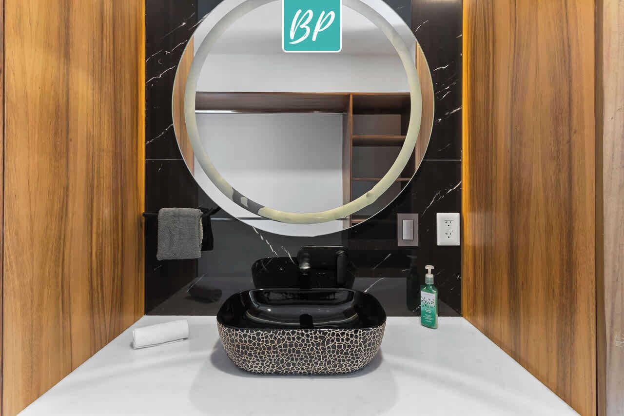 A bathroom with a round mirror, a sink with a patterned basin, a towel, and a soap dispenser.