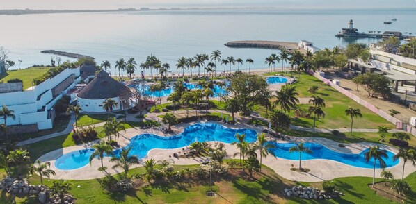 Eine Luftaufnahme eines Resorts mit mehreren Schwimmbecken, Palmen und direktem Strandzugang.