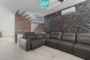 Una sala de estar moderna con un sofá seccional, una escalera de peldaños de madera y una pared de piedra texturizada.