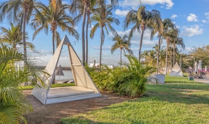 A grassy area with a pyramid-shaped structure, palm trees, and a lighthouse in the background.