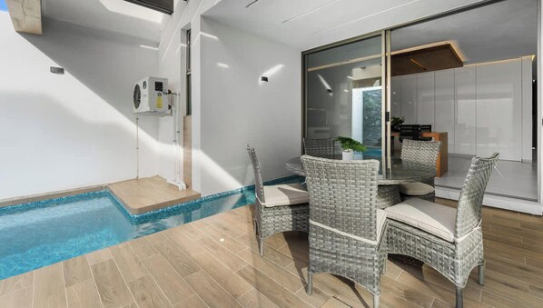 A modern indoor pool area with a glass wall, wicker chairs, and a small table. - Villa 83: 3BR, 2 Private Pools & Beach Club Access (Cruz de Huanacaxtle)