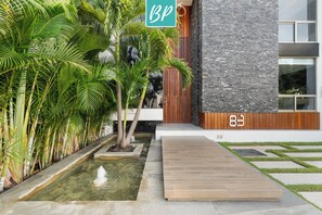 A modern building with a stone facade, a wooden deck, and a water feature with palm trees. - Villa 83: 3BR, 2 Private Pools & Beach Club Access (Cruz de Huanacaxtle)