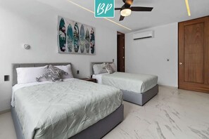 Ein Schlafzimmer mit zwei Betten, einem Deckenventilator, einer wandmontierten Klimaanlage und einer Holztür.