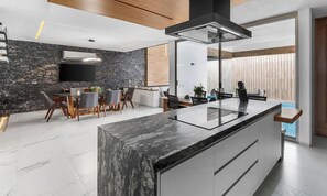 A modern kitchen with a marble island, a dining area with a table and chairs, and a large window with blinds.
