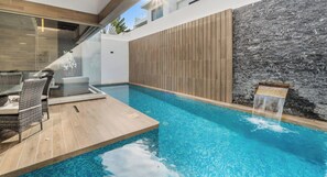 A modern outdoor pool area with a wooden deck, lounge chairs, and a stone wall.