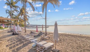 Ein Strand mit Liegestühlen, Sonnenschirmen und Palmen.