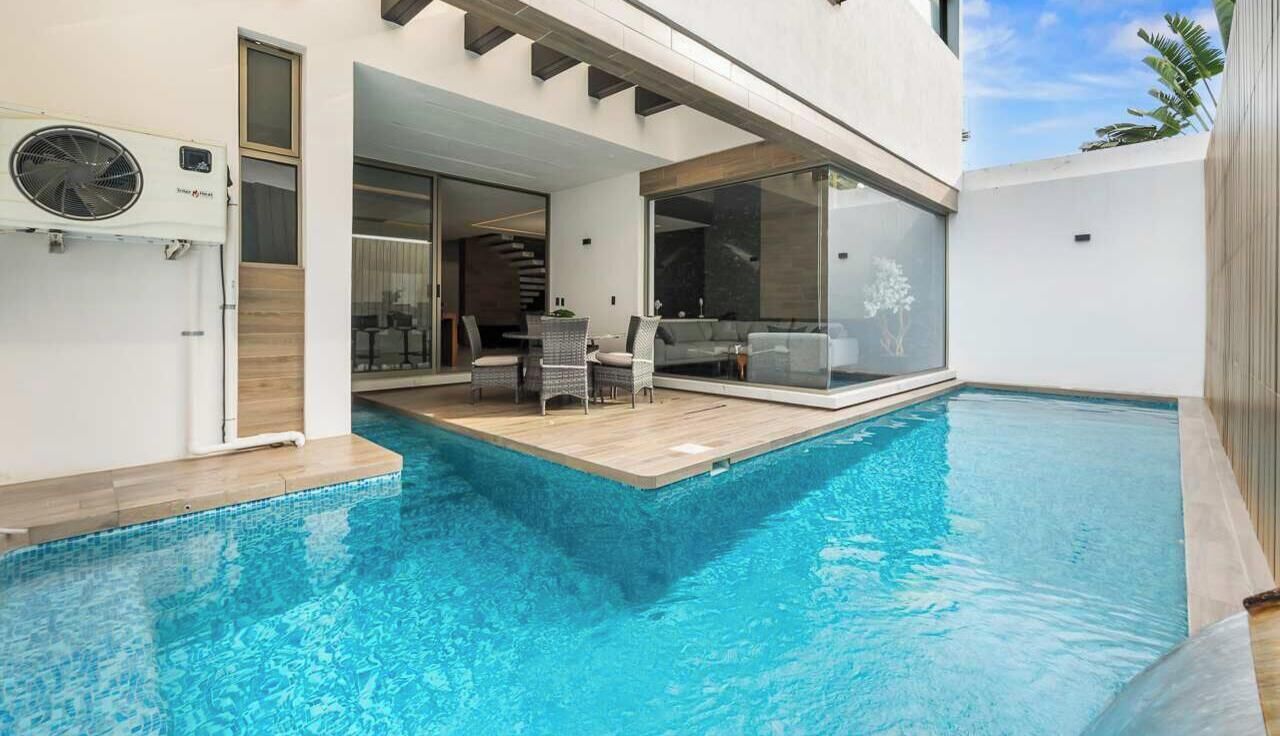 Un área de piscina moderna al aire libre con una zona de estar integrada y un acceso interior mediante una puerta corrediza de vidrio.