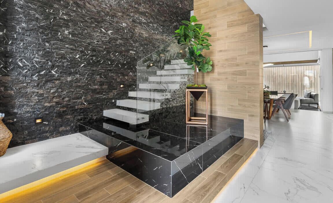 Un interior moderno con una pared de mármol negro, una escalera y un piso de madera.