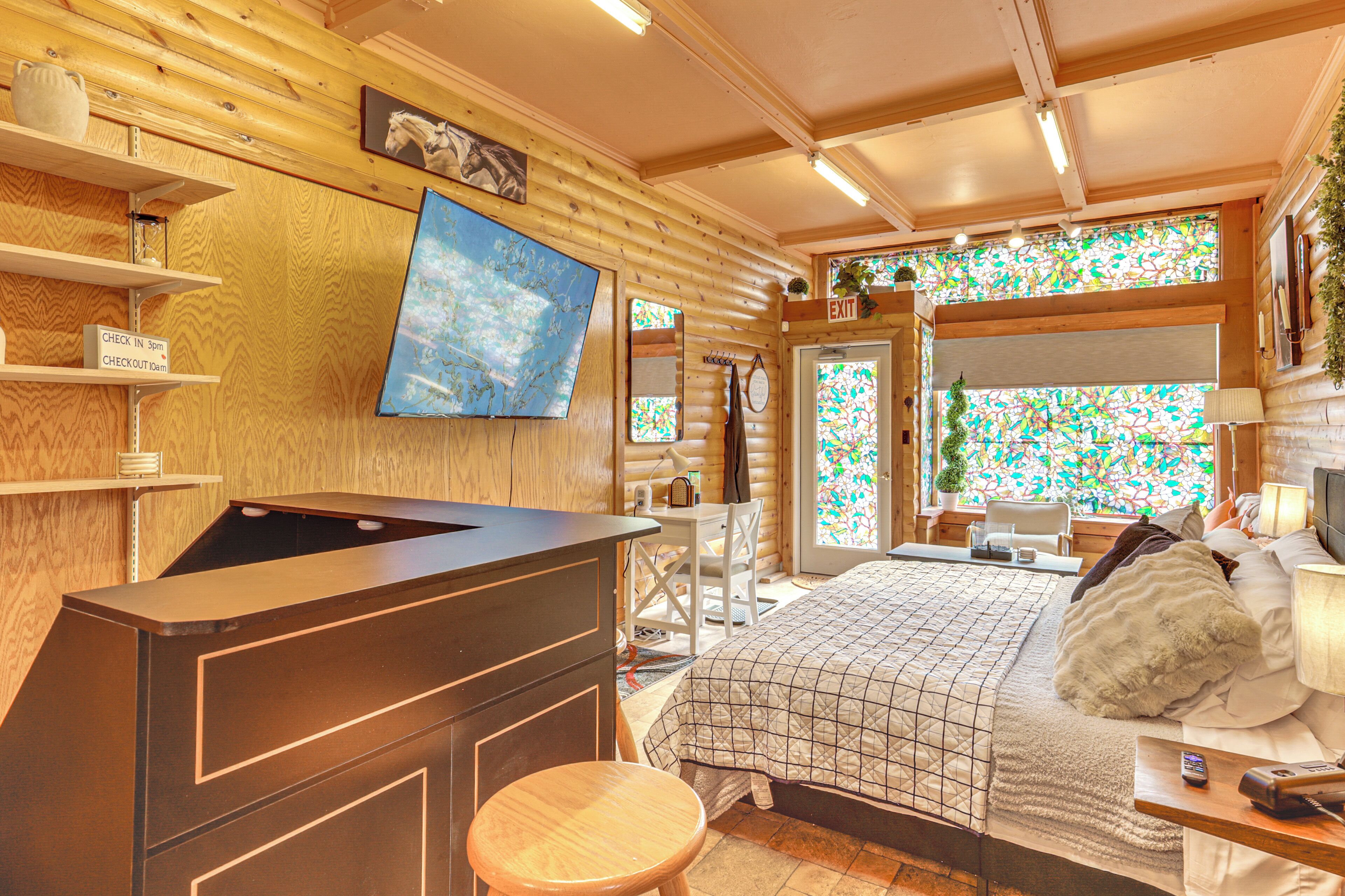 Une pièce aménagée dans le style d’un chalet en rondins, avec un lit, un bureau et une grande fenêtre ornée de vitraux.