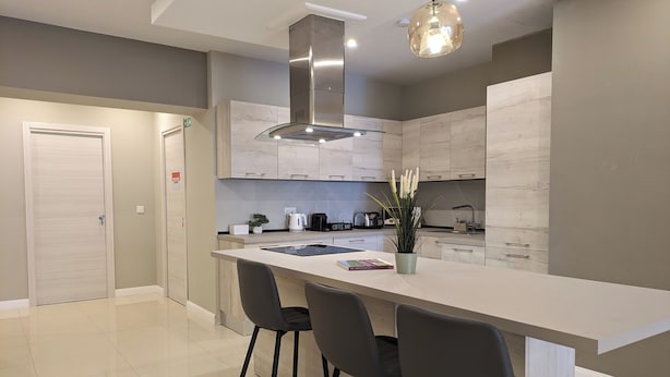 A modern kitchen with a central island, bar stools, a coffee machine, and a hanging light fixture.
