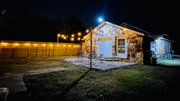 Un edificio de piedra con un pequeño patio, mobiliario exterior e iluminación con luces colgantes.