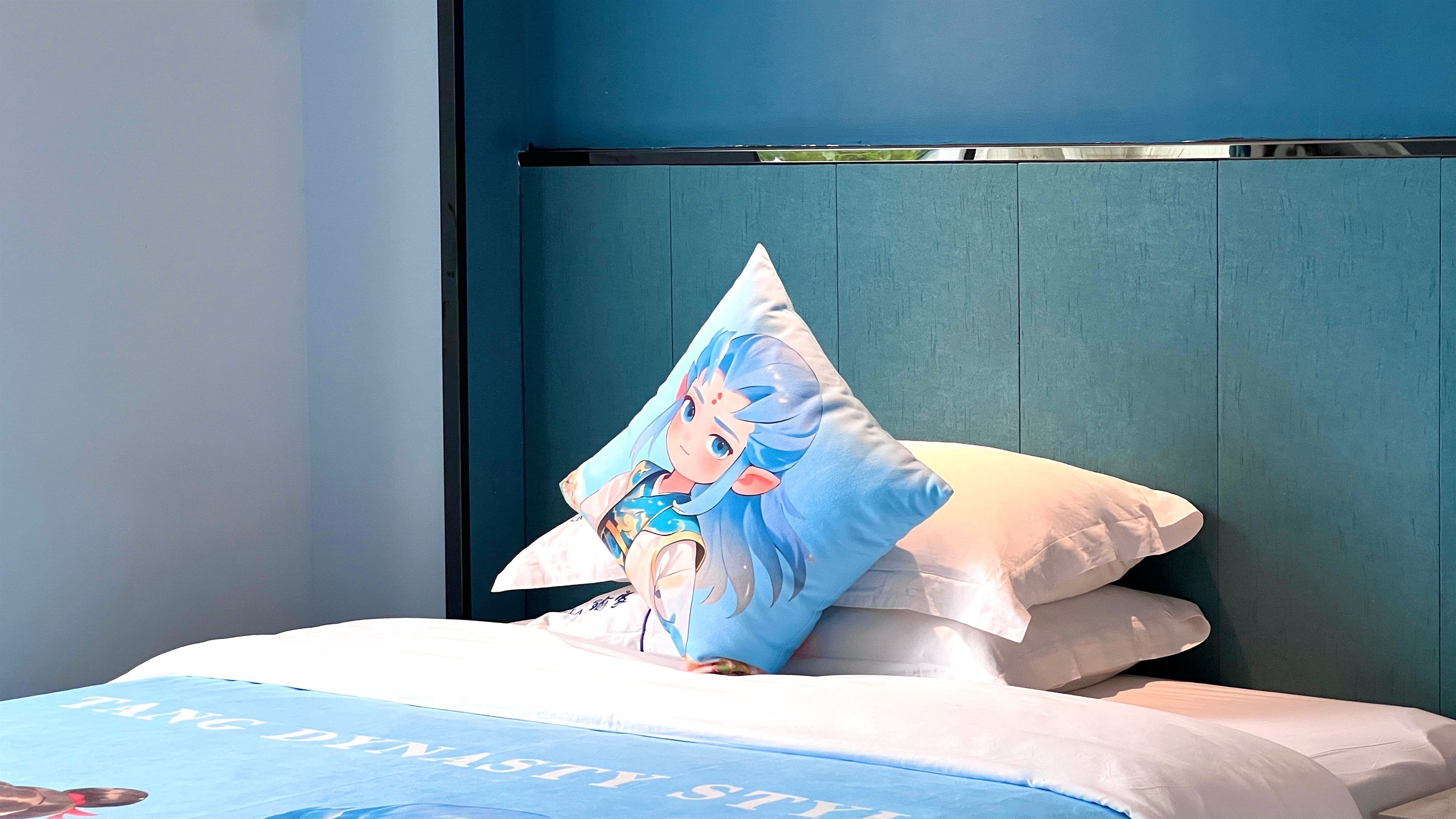 A bed with a blue and white bedding set, a pillow with a character design, and a teal-colored headboard.