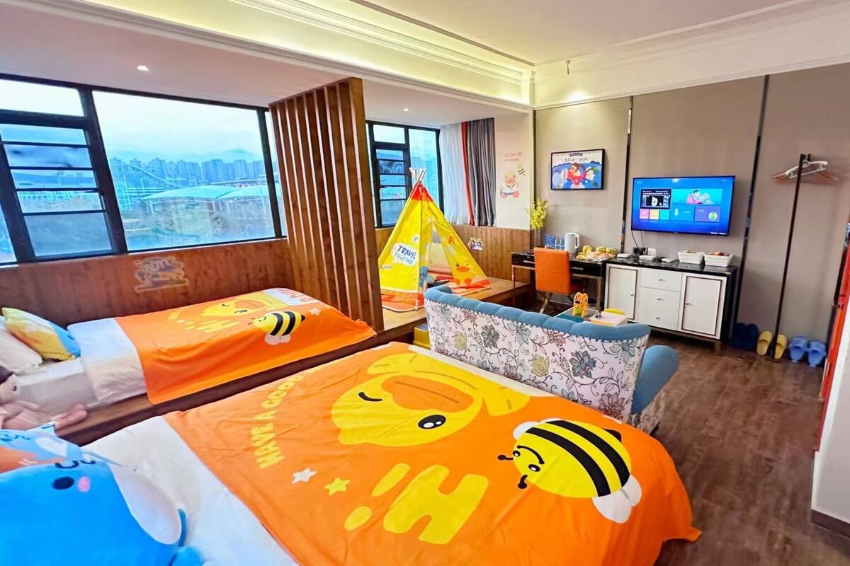 A hotel room with two beds, a desk, a television, and a view of a cityscape.