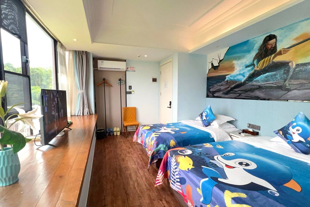 A hotel room with two beds, a TV, a plant, and a painting on the wall.