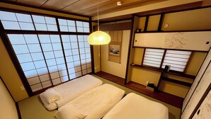 Una habitación tradicional japonesa con suelo de tatami, dos camas individuales, un farol de papel colgante y una ventana con celosía shoji.