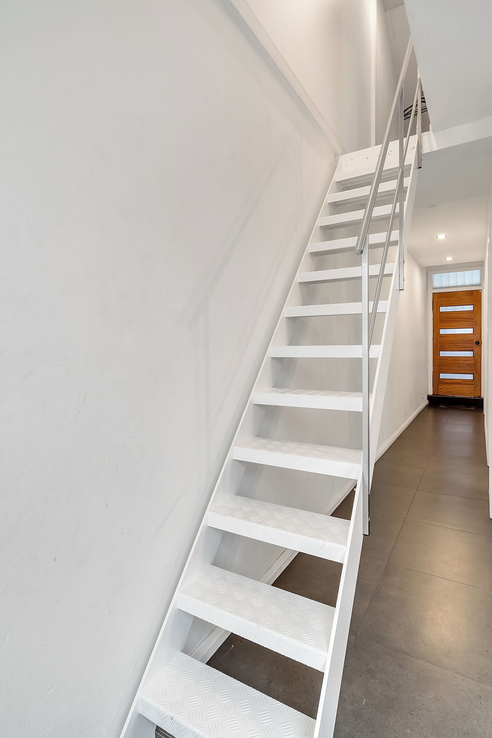 A white staircase with a metal railing leading to a wooden door.