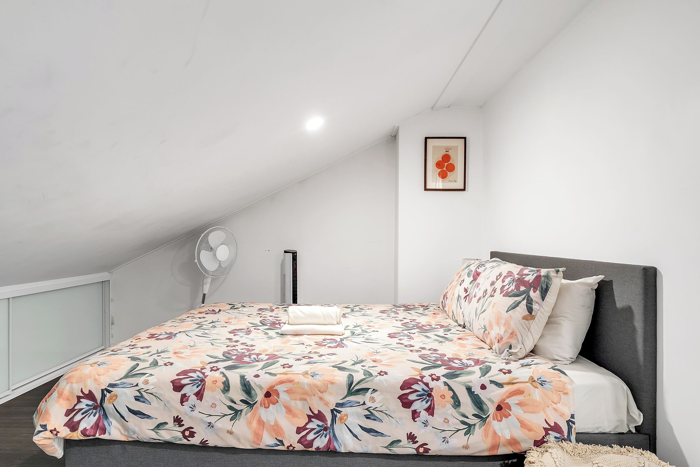 Quarto com colcha florida, cabeceira cinza e quadro pendurado na parede.