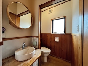 A bathroom with a wooden vanity, a round mirror, a toilet, and a window. - hitahostel (Hita)