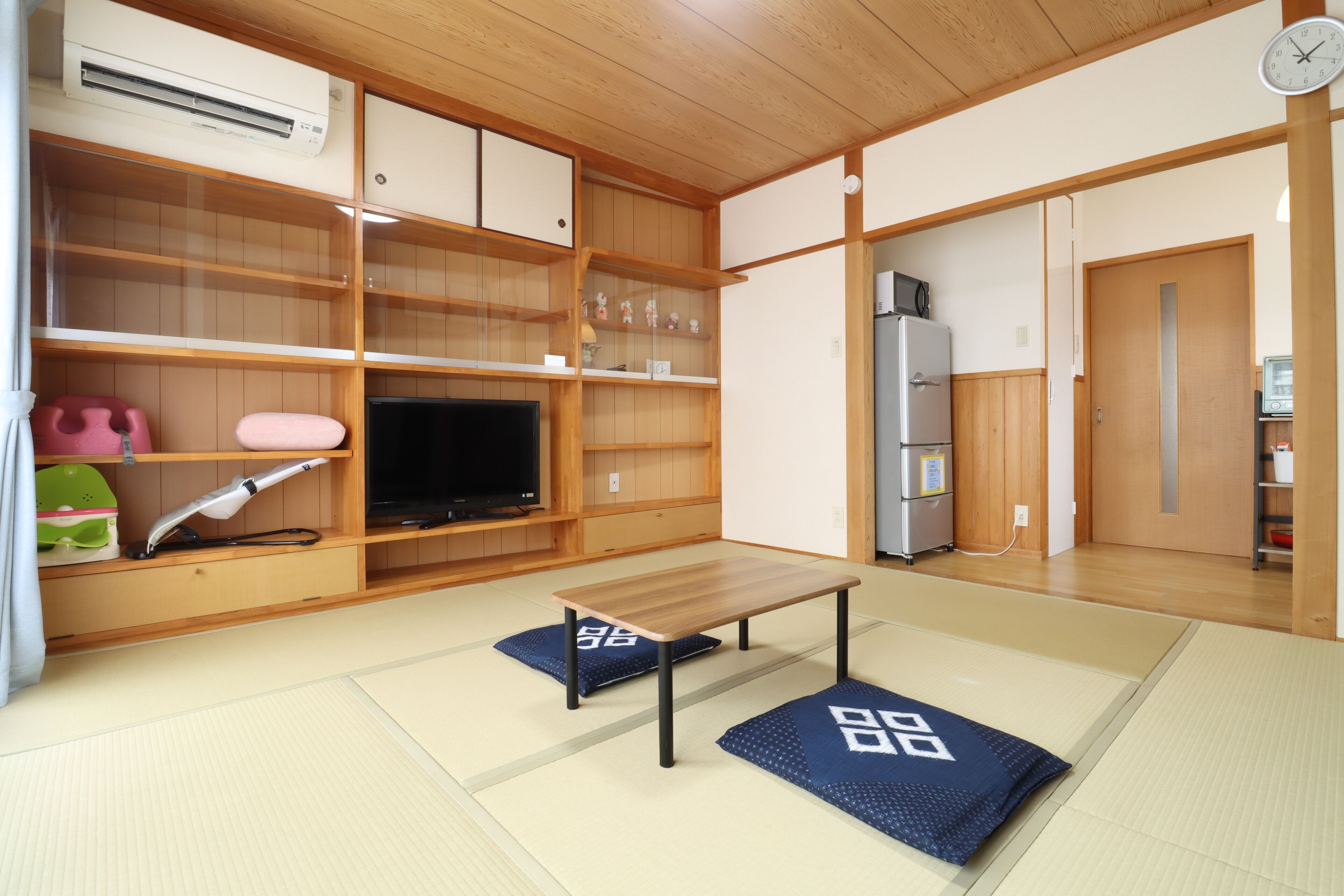 A traditional Japanese room with tatami flooring, a television, a refrigerator, and wooden shelves.