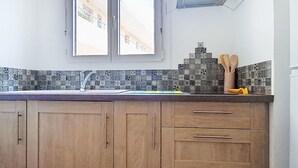 A kitchen with wooden cabinets, a tiled backsplash, and a window above the sink. - La siesta by Interhome (Six Fours)
