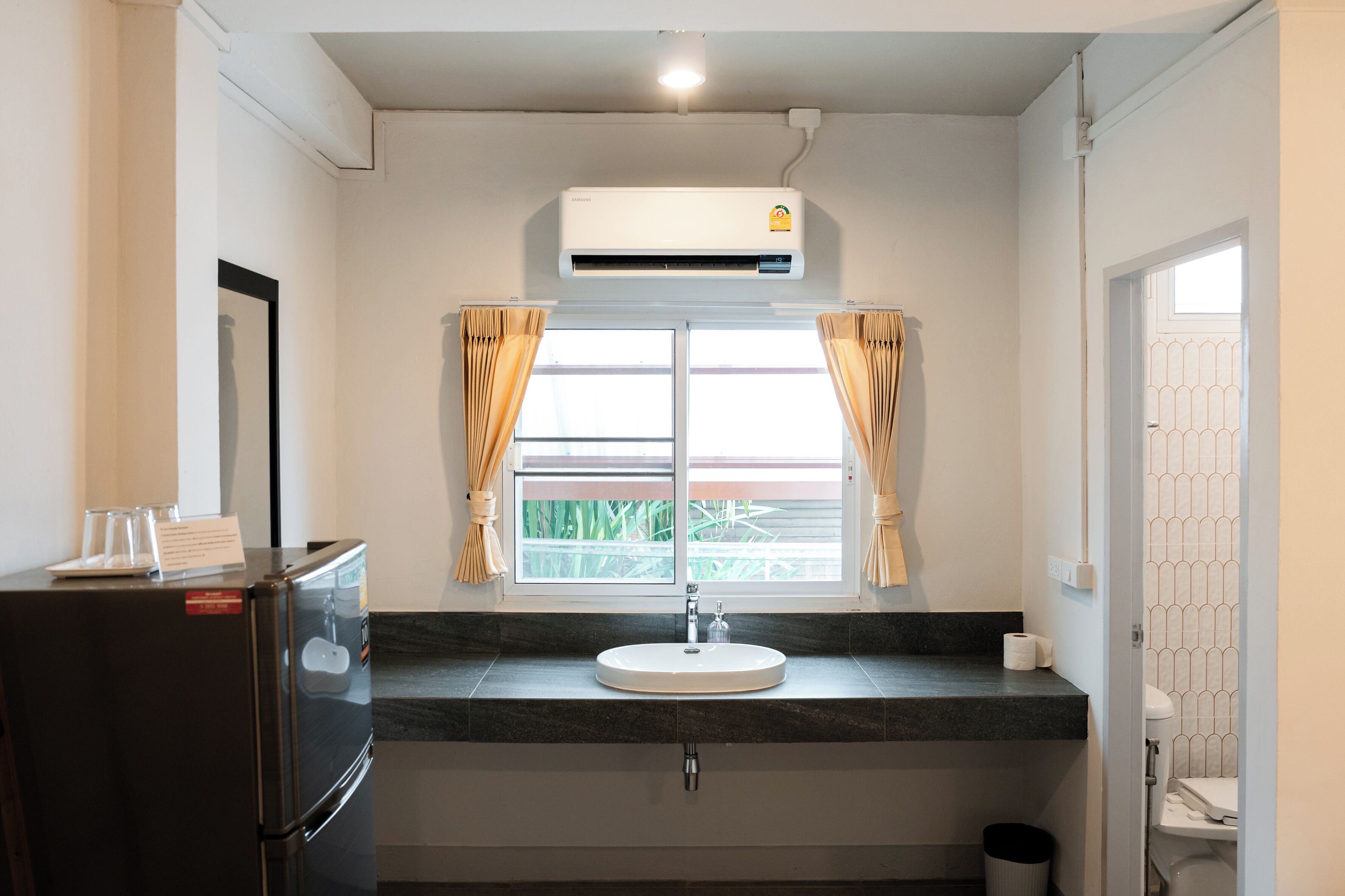 Casa de banho com lavatório, espelho, janela com cortinas e ar condicionado.