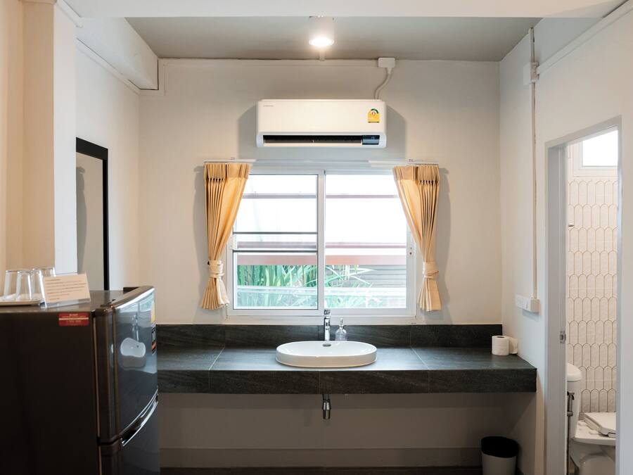 Casa de banho com lavatório, espelho, janela com cortinas e ar condicionado.