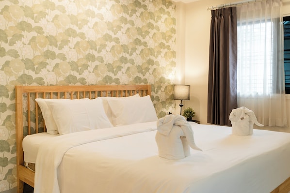 A neatly made bed with white linens, a wooden headboard, and two towels on the bed.