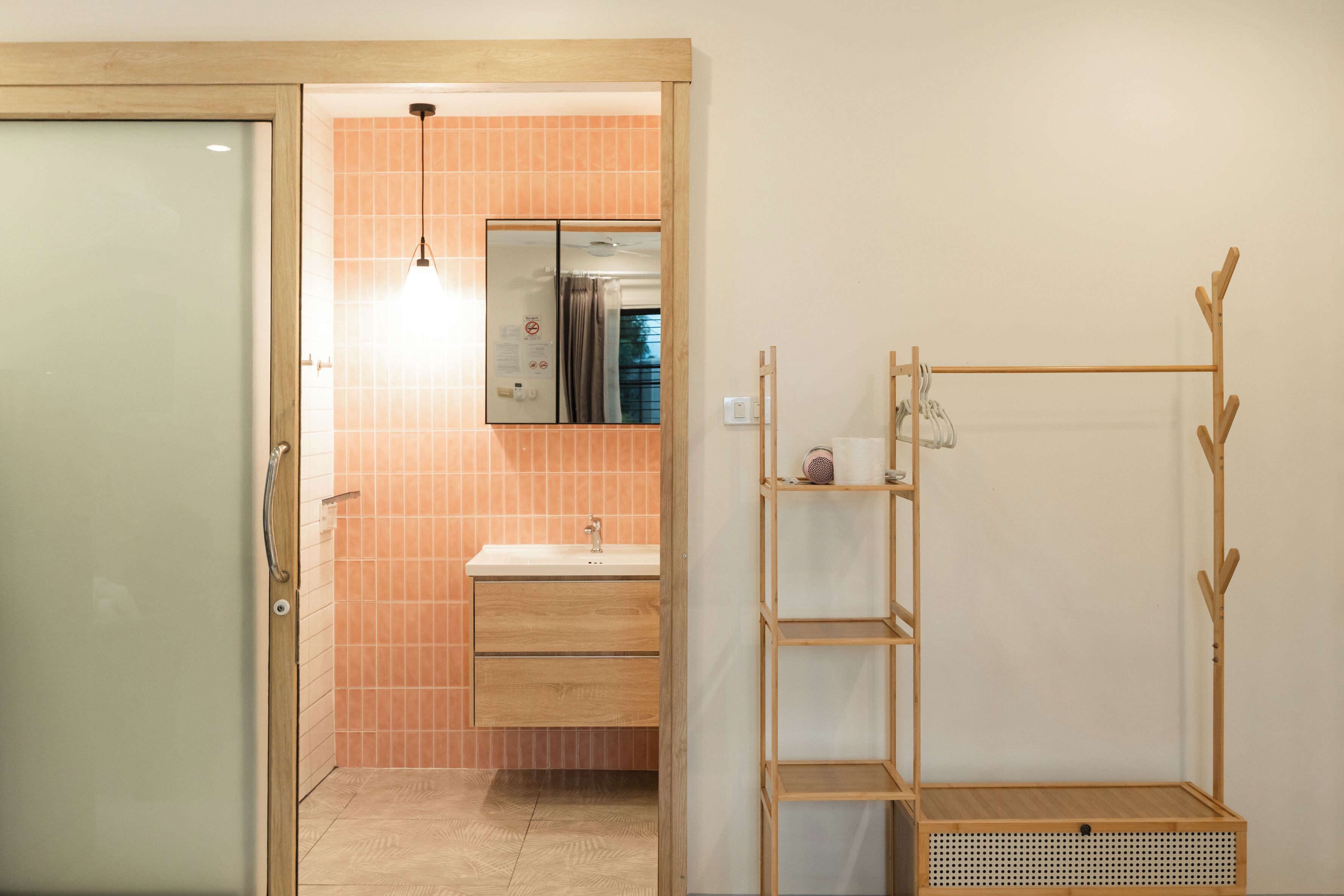 A bathroom with a glass door, a sink, a mirror, and a wooden rack.