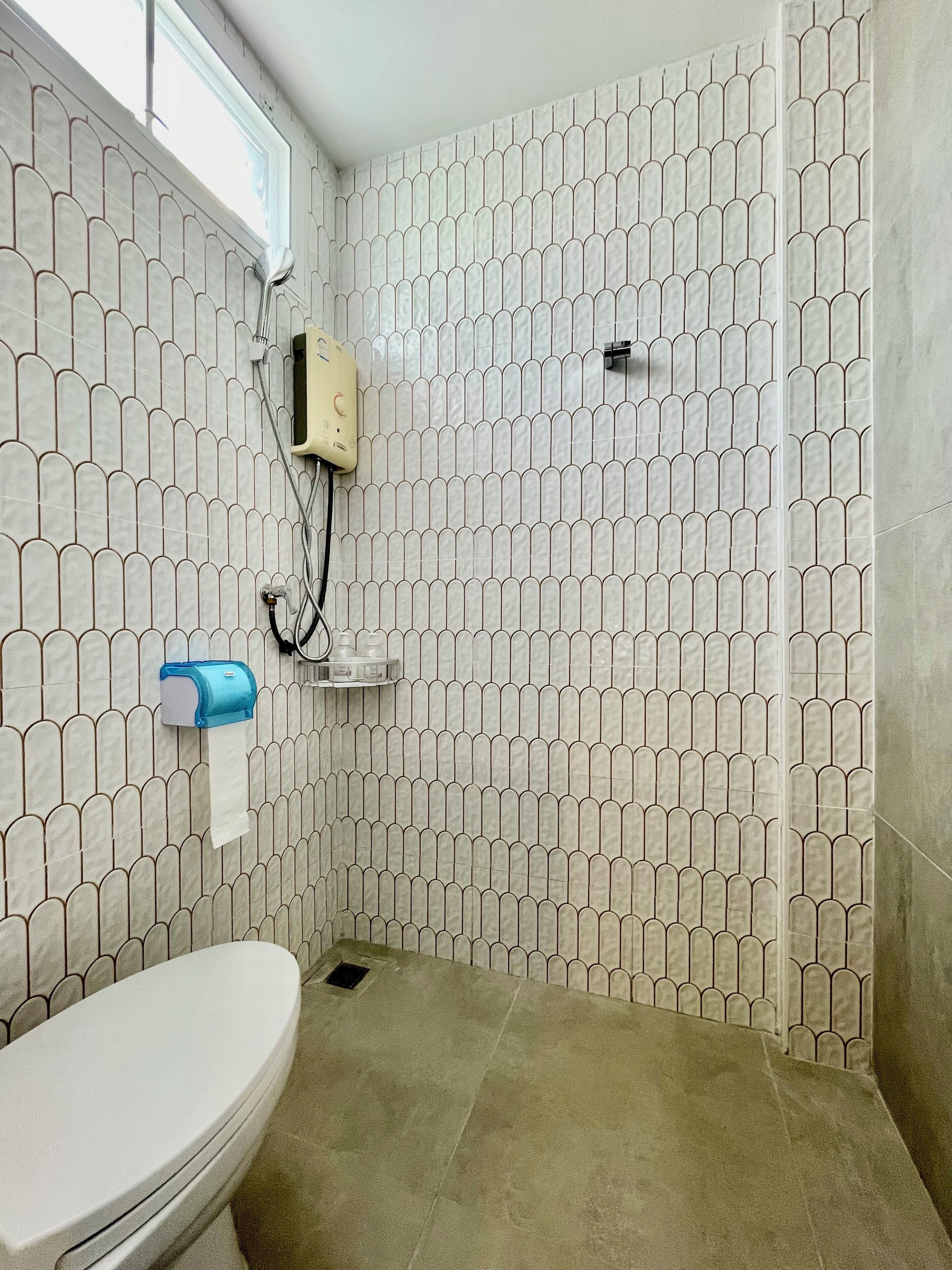 A bathroom with a toilet, a towel dispenser, and a shower area with a tiled wall.