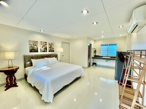 A hotel room with a large bed, bedside tables, a desk, a chair, a window, and an air conditioning unit.