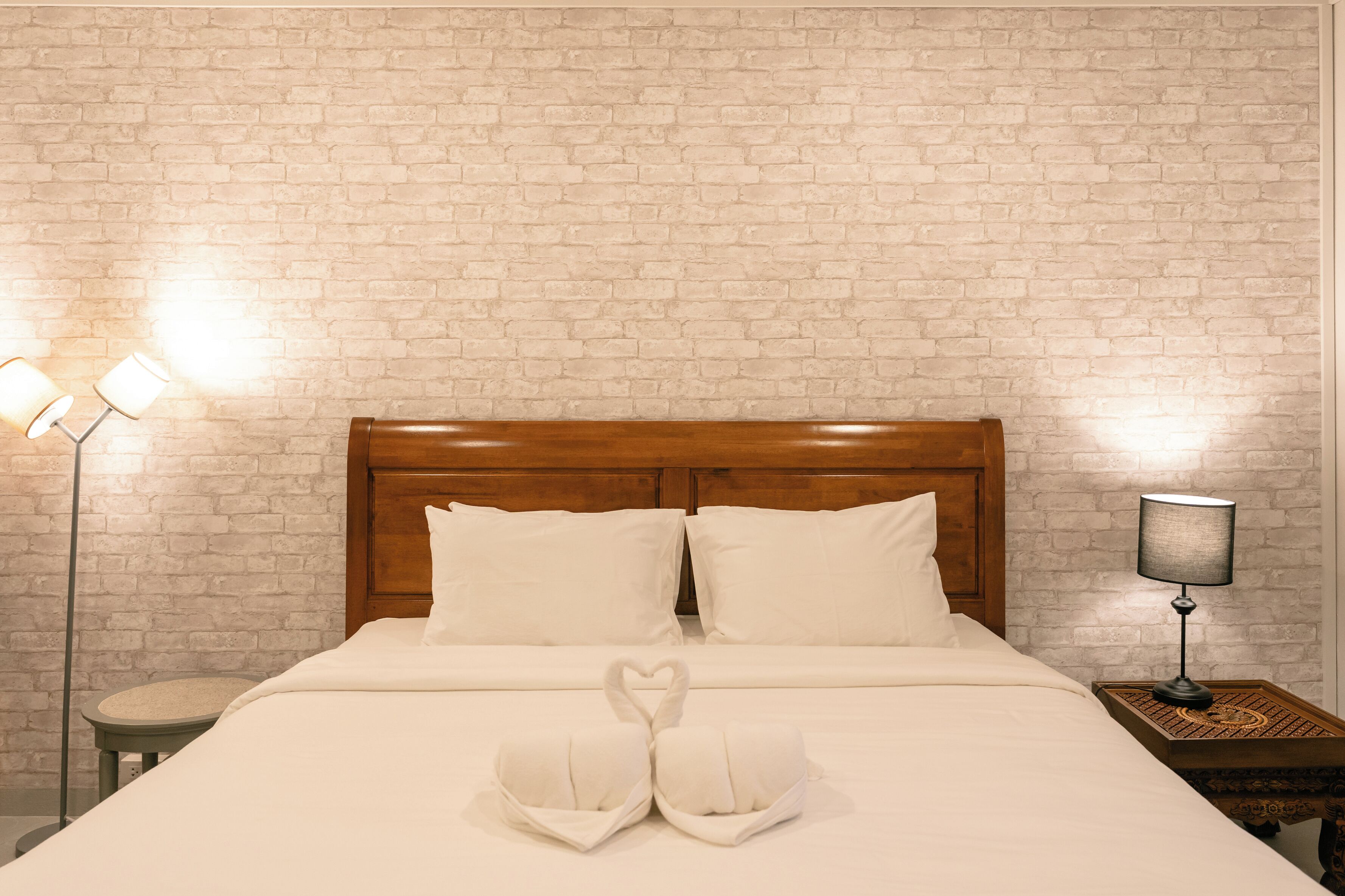 Een hotelkamer met een metselwerkmuur, een houten hoofdbord, een bed met wit beddengoed, twee nachtlampjes en een decoratieve zwaan op het bed.