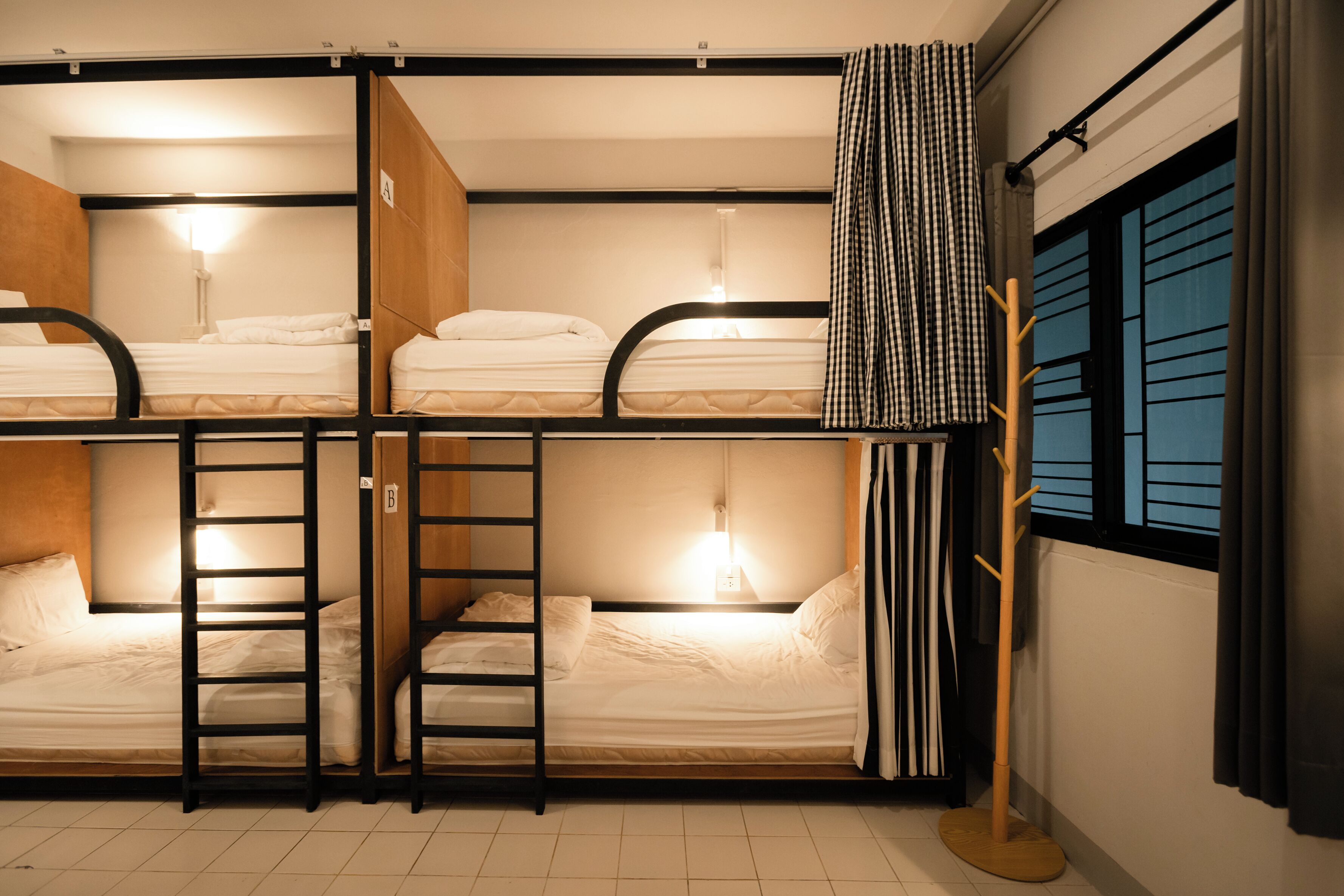 Habitación con literas, una escalera, una ventana con cortinas y un perchero.
