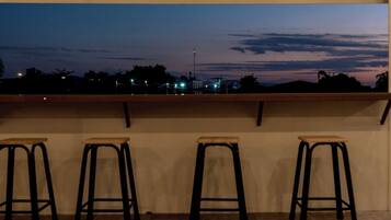 A balcony with three wooden stools and a view of a cityscape at dusk.