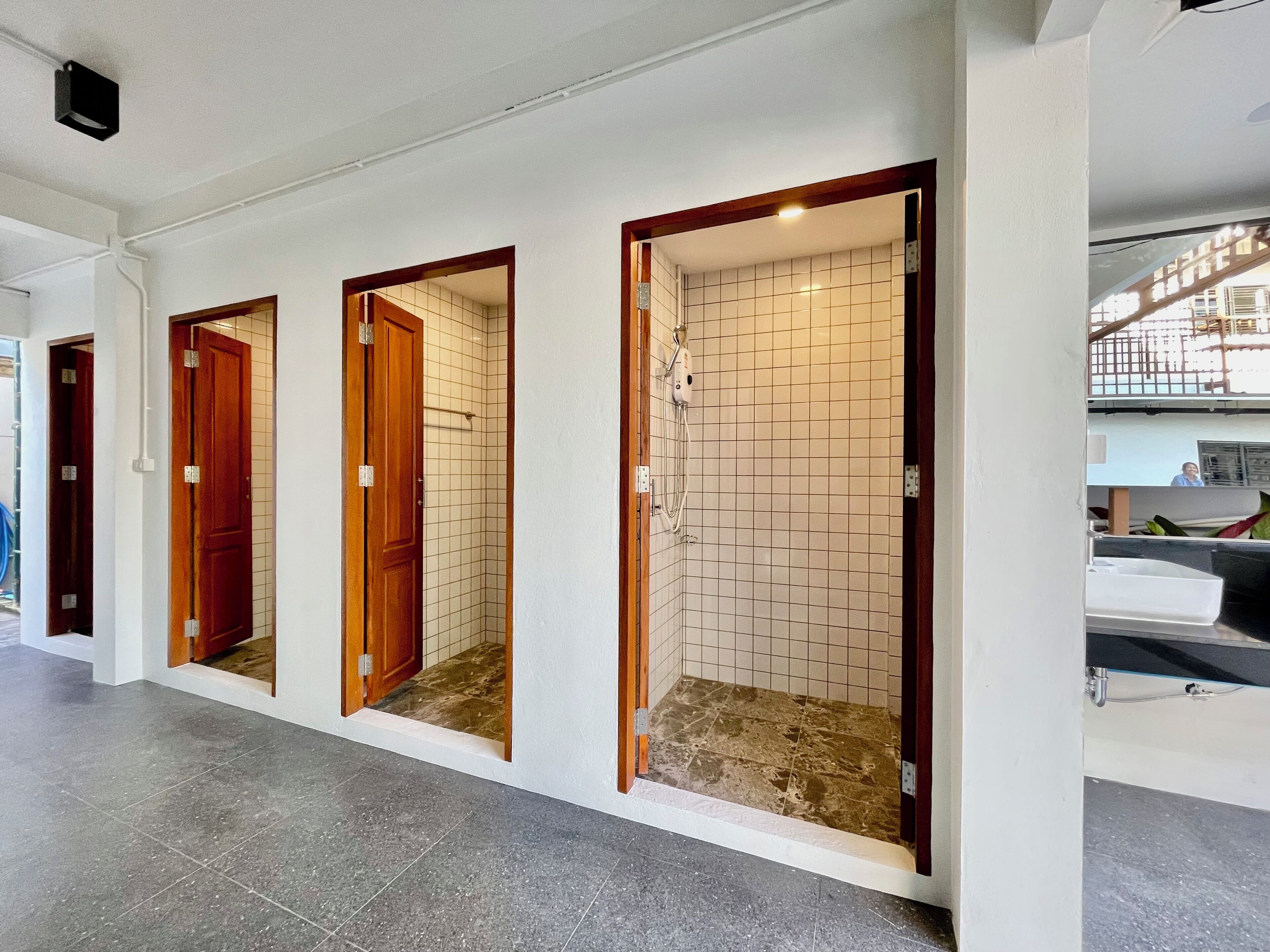 A hallway with three wooden doors leading to individual rooms, each with a tiled shower area.