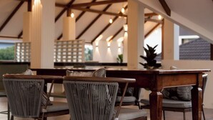 An outdoor seating area with wooden tables and wicker chairs, under a high ceiling with exposed beams and hanging lights. - Secret Corner Boutique Stay  (Chiang Rai)